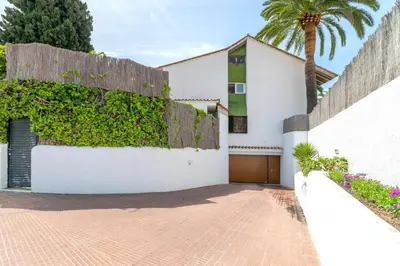 a white house with a fence and a palm tree at Paola: Preciosa casa pareada con piscina in Sitges