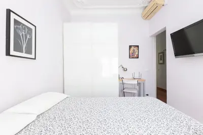 a white bedroom with a bed and a flat screen tv at ApartEasy - Modernist flat in Eixample center in Barcelona