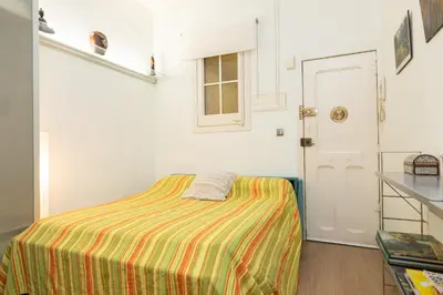 a small room with a bed with a striped blanket at ApartEasy - Central Barcelona Studio Apartment in Barcelona