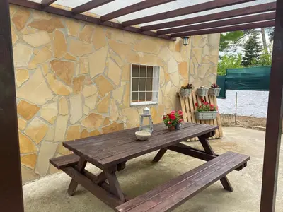 a wooden picnic table with a bench and a stone wall at Casita rural con piscina in La Torre de Claramunt