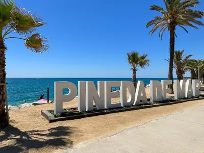 a sign on the beach with palm trees and the ocean at Vivalidays Vianka - Pineda de Mar in Pineda de Mar