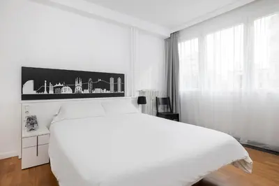 a white bedroom with a large white bed and a window at La Mejor Zona de Barcelona in Barcelona
