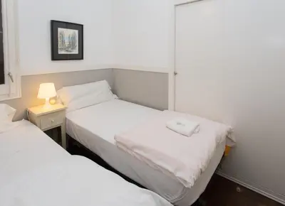 two beds in a small room with a lamp on a table at Letsgo Camp Nou Apartment in Barcelona
