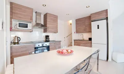 a kitchen with wooden cabinets and a bowl of fruit on a counter at Modern Duplex in Sitges with Private Parking, Sea Views & Terrace in Sitges