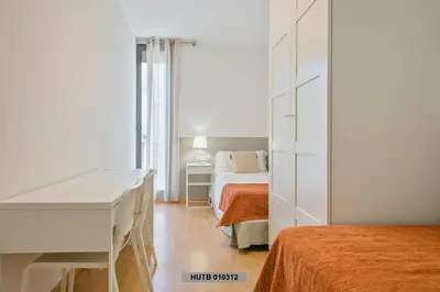 a white bedroom with a bed and a desk in it at Alcam Glorias in Barcelona