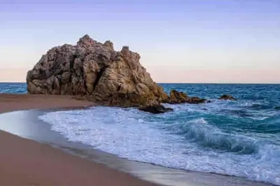 a large rock in the ocean next to a beach at Apartamento “La Caleta” in Calella