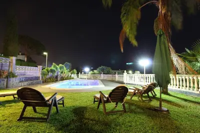 a group of chairs sitting next to a pool at night at Basketball court, pool, BBQ, gardens, seaviews in San Pol de Mar