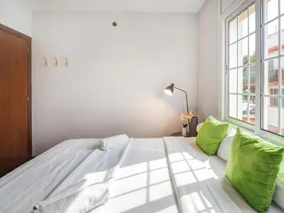 a white bedroom with a large bed with green pillows at The Beach Apartment by Hello Homes Sitges in Sitges