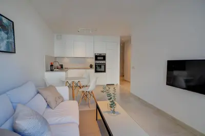 a living room with a white couch and a kitchen at Camelot Apartment by Hello Homes Sitges in Sitges