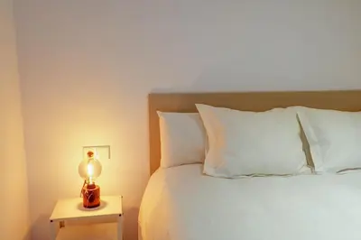 a bed with white pillows and a lamp on a table at Camelot Apartment by Hello Homes Sitges in Sitges