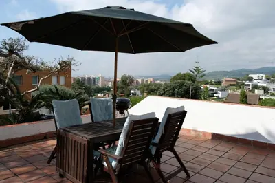 a table and chairs under an umbrella on a patio at Casa familiar en la playa con piscina in Teià