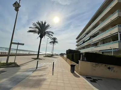 a sidewalk next to a beach with palm trees and a building at Cunit Beach in Cunit
