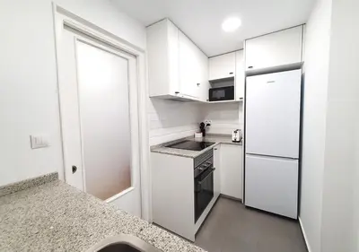a small kitchen with white cabinets and a refrigerator at Acojedor piso cerca del metro in Cornellà de Llobregat