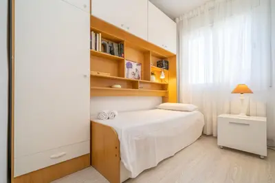 a small bedroom with a white bed and wooden shelves at HomeHolidaysRentals Bluemar-Costa Barcelona in Pineda de Mar
