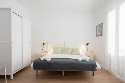 a white bedroom with a bed and two lamps at Housalia Lepant 3 bedroom apartment 300 meters de Sagrada Familia in Barcelona