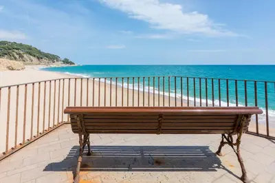 a wooden bench sitting on a balcony overlooking the beach at HomeHolidaysRentals Ancora - Costa Barcelona in San Pol de Mar