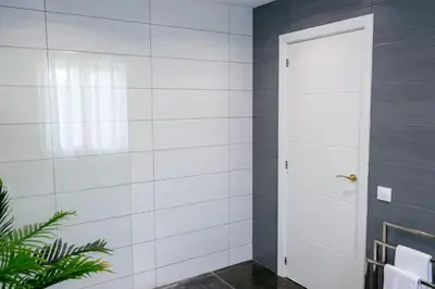 a bathroom with a white tiled wall and a door at VILLA 5 PLAYA A 2 MINUTOS in Castelldefels