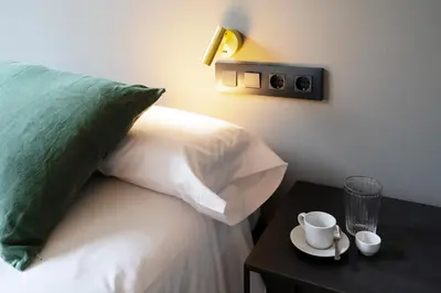a bed with a green pillow and a table with a cup at Hostal Porxos Garden in Barcelona