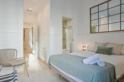 a white bedroom with a bed and a chair at Anton's Downtown Apartment in Barcelona
