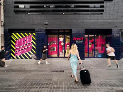 a woman walking down a street with a suitcase at AMISTAT City Hostel Barcelona in Barcelona