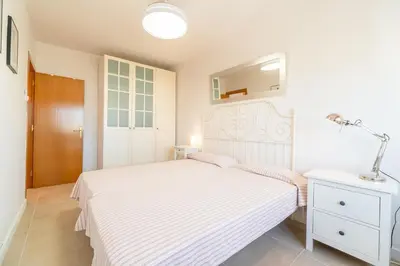 a white bedroom with a bed and a lamp on a table at Horizonte Azul Sitges in Sitges