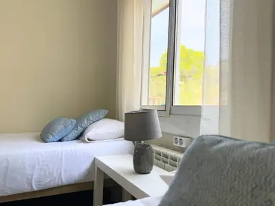 a bedroom with two beds and a window and a chair at Atico Isabel in Castelldefels