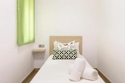 a small bedroom with a bed with white sheets and pillows at El balcón de Sagrada Familia in Barcelona