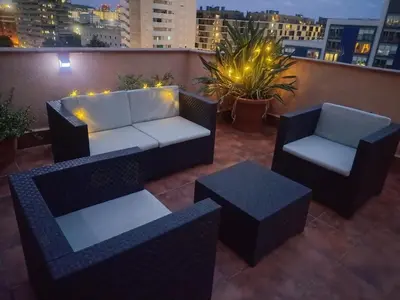 a rooftop patio with a couch and chairs and lights at Cozy and sunny penthouse Fira BCN in Hospitalet de Llobregat