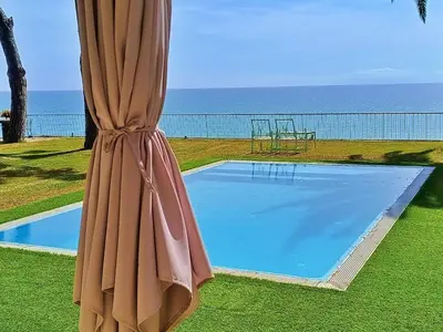 a large pool with an umbrella next to aophe at Preciosa casa al borde de un acantilado in Arenys de Mar