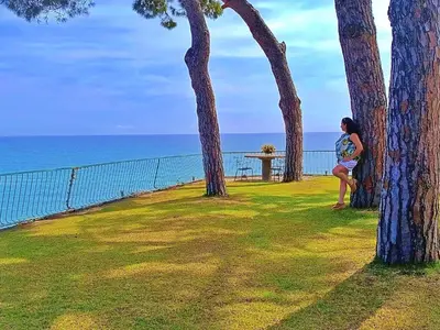 a woman sitting between two trees next to the ocean at Preciosa casa al borde de un acantilado in Arenys de Mar