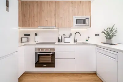 a white kitchen with wooden cabinets and a sink at Limehome Barcelona Plaça Pirineus in Hospitalet de Llobregat