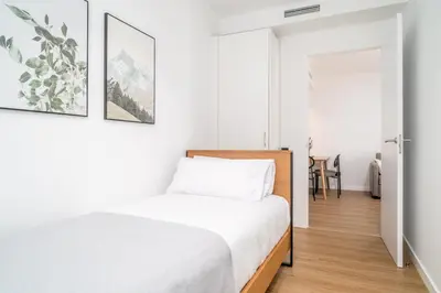 a white bedroom with a bed and a table at Limehome Barcelona Plaça Pirineus in Hospitalet de Llobregat