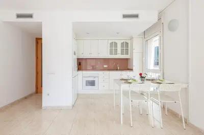 a kitchen with white cabinets and a table and chairs at Nova Apartment by Hello Homes Sitges in Sitges