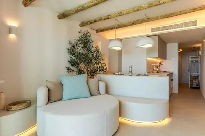 a living room with a white chair and a kitchen at Apartamentos Azul in Castelldefels