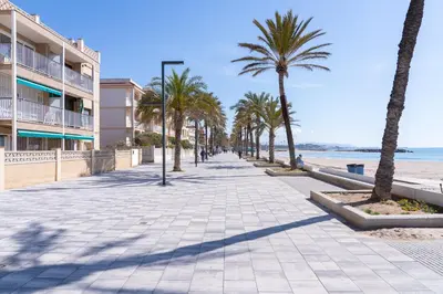 a sidewalk next to the beach with palm trees at Hauzify I Apartament Zulú Cubelles in Cubelles