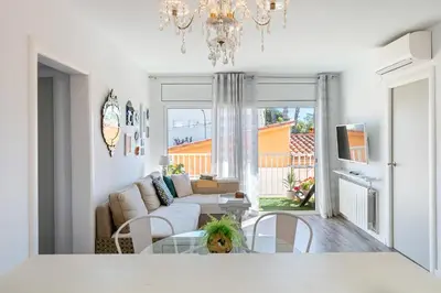 a white living room with a chandelier and a table at Hauzify I Apartament Zulú Cubelles in Cubelles