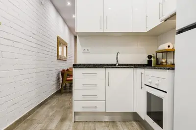 a kitchen with white cabinets and a white brick wall at Novus Homes Barcelona Santa Eulalia in Hospitalet de Llobregat
