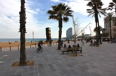 a beach with palm trees and people sitting on benches at ClassBedroom Barcelona Beach Apartments in Barcelona