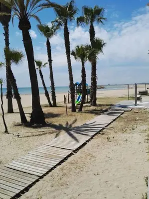 a sandy beach with palm trees and a playground at Apartamento Sunny Home in Cunit