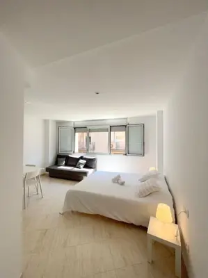 a white bedroom with a bed and a living room at M2 Apartament cèntric in Terrassa