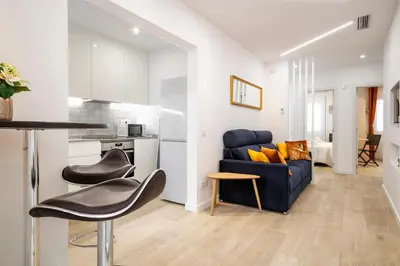 a living room with a blue couch and a kitchen at Boutique Plaza Catalonia Suites Cornellá in Cornellà de Llobregat