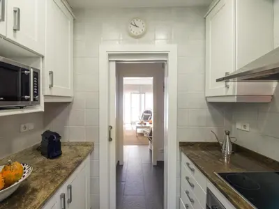 a kitchen with white cabinets and a clock on the wall at Apartamento cómodo frente al mar con acceso directo a la playa - ES-332-6 in Vilanova i la Geltrú