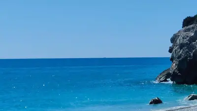 a beach with blue water and a rocky cliff at Ànima del Garraf in Sitges