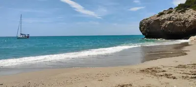 a sandy beach with a sail boat in the ocean at Ànima del Garraf in Sitges