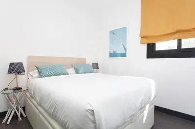 a white bed with blue pillows in a bedroom at Cómodo apartamento para dos en el Eixample in Barcelona