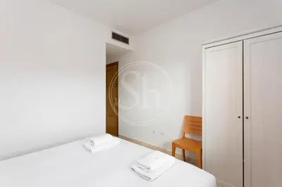 a white bedroom with two beds and a chair at Apartamento para 3 con balcón in Barcelona