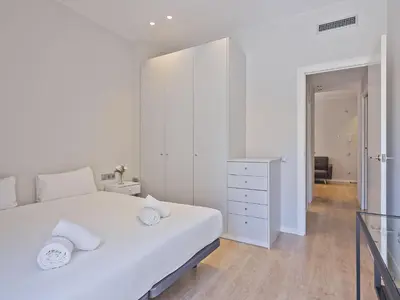 a white bedroom with a large white bed and a dresser at Ola Living Gracia in Barcelona