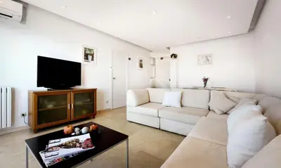 a living room with a white couch and a tv at Sitges Apartamente frente al mar con piscina in Sitges