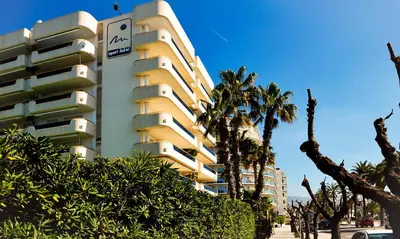 a tall yellow building with palm trees in front of it at Sitges Apartamente frente al mar con piscina in Sitges