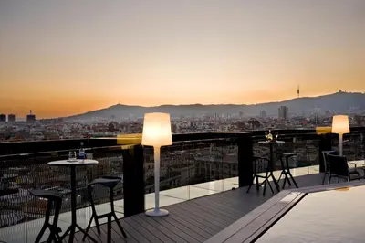 a rooftop bar with tables and chairs and a view of a city at Barceló Raval in Barcelona